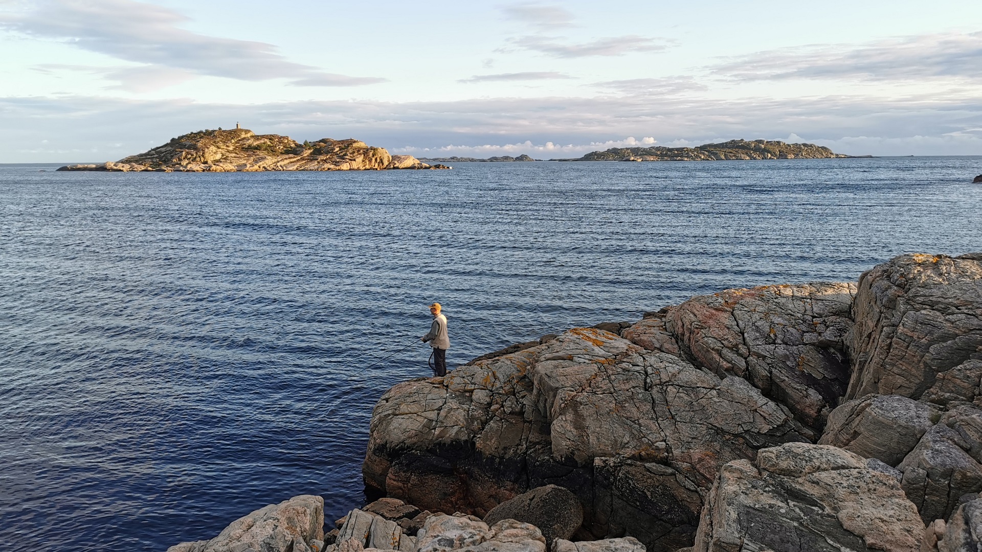 Ein Mann beim Angeln vom felsigen Ufer in der Lussevika bei Åvik gegenüber der vorgelagerten Inseln