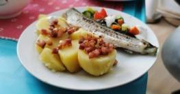 Kartoffeln mit Speckwürfeln und bunter Salat mit selbstgemachtem Knoblauchdip flankieren ein kross gebratenes Stück Hornhecht auf einem weißen Teller
