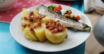 Kartoffeln mit Speckwürfeln und bunter Salat mit selbstgemachtem Knoblauchdip flankieren ein kross gebratenes Stück Hornhecht auf einem weißen Teller