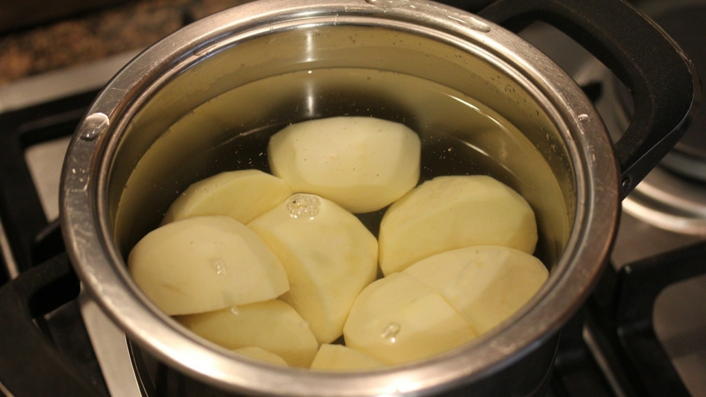 Ein Topf mit Wasser und teils geviertelten, teils halbierten Kartoffeln steht auf einer Herdplatte