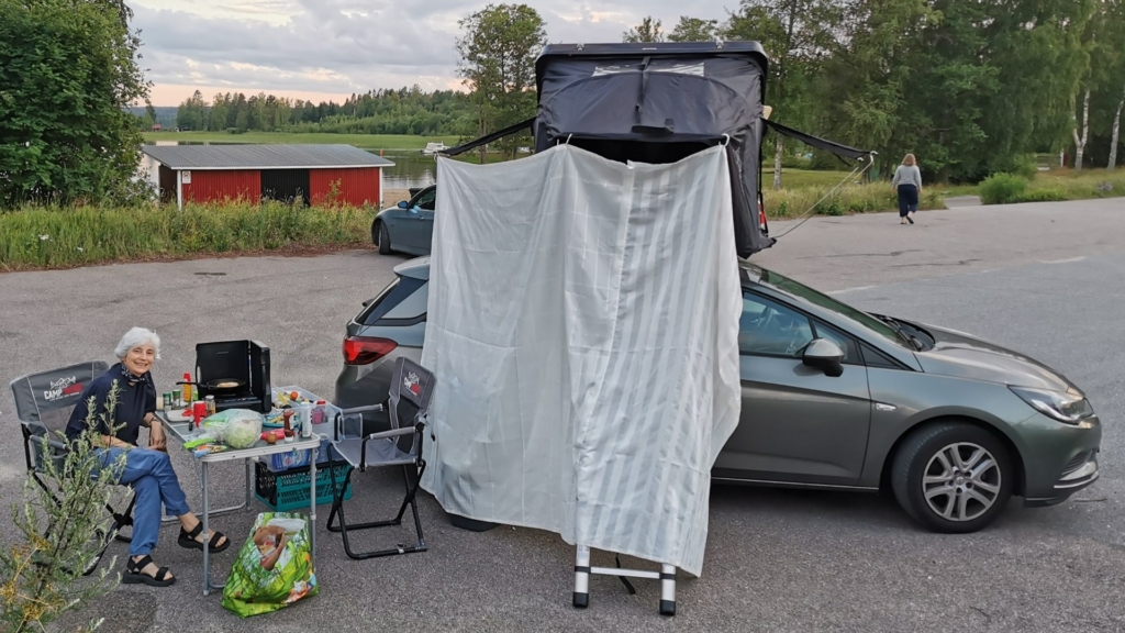 Ein Duschvorhang ist in ein Dachzelt eingeklippt und bildet einen pragmatischen, günstigen, wenn auch optisch nicht ganz ansprechenden Sichtschutz für ein mobiles WC beim Angeln mit Dachzelt