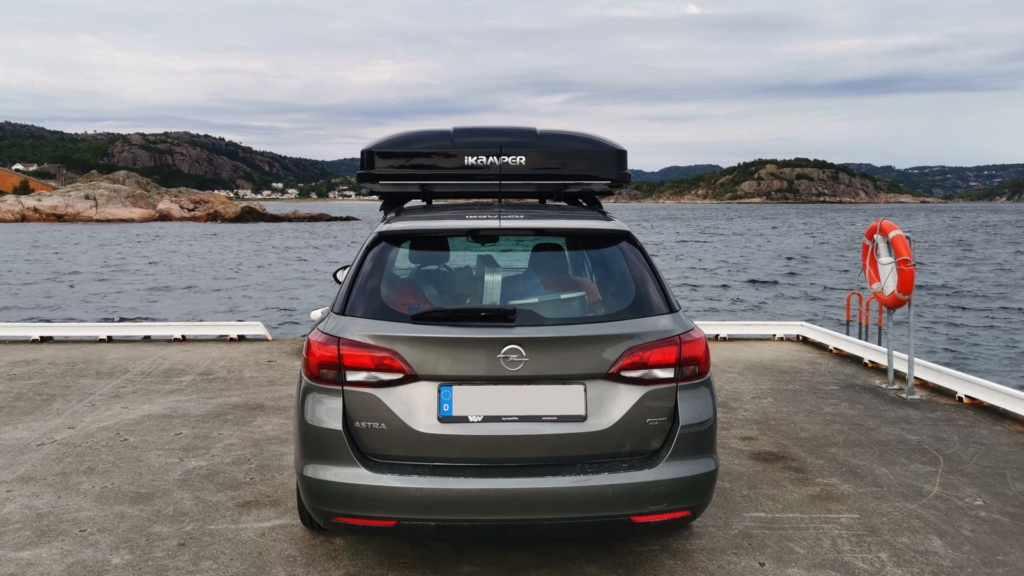 Angeln mit Dachzelt - Ein Opel Astra K Sports Tourer mit einem verschlossenen iKamper Skycamp 3.0 Mini auf dem Dach steht auf der Kaimauer einer Anlegestelle in der Nähe von Lyngdal