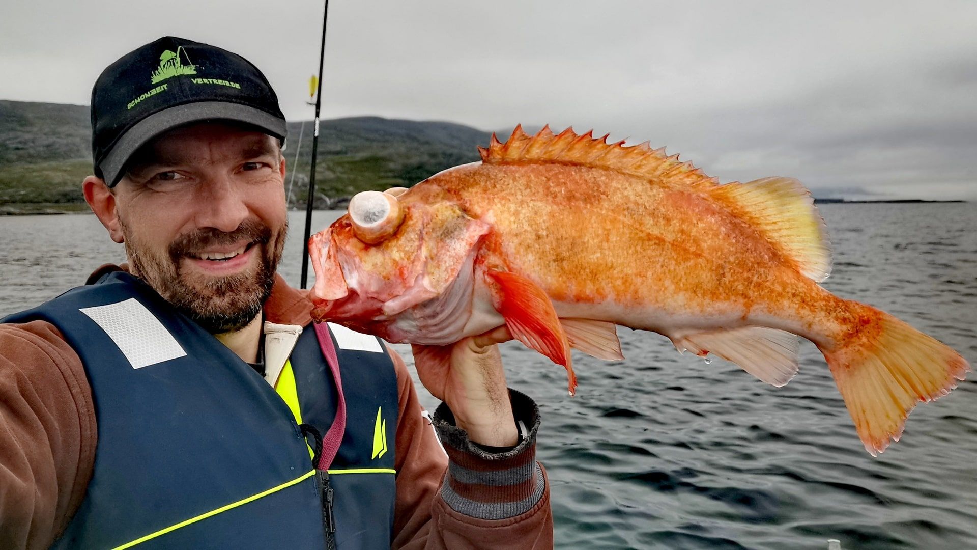 Ein Angler zeigt stolz einen kapitalen Rotbarsch, gefangen beim Angeln im Akkarfjord vom Boot aus – typische Merkmale nach dem Drill aus der Tiefe sichtbar.