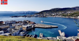 Blick auf die Stellen zum Angeln am Kreuzfahrt-Hafen von Hammerfest, blauer Himmel und tiefblaues Wasser mit einem Schiff, das den Hafen verlässt