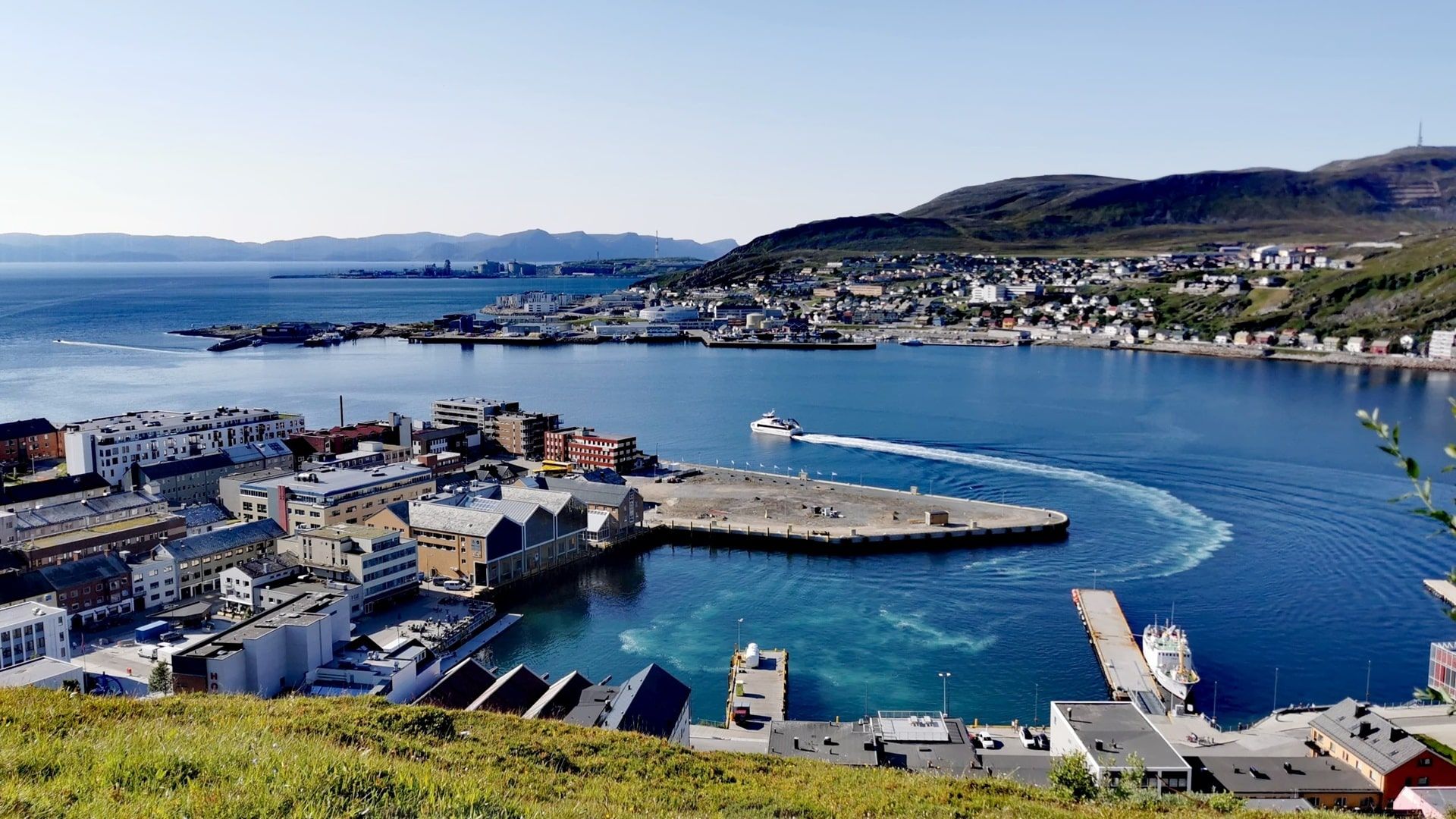 Blick auf die Stellen zum Angeln am Kreuzfahrt-Hafen von Hammerfest, blauer Himmel und tiefblaues Wasser mit einem Schiff, das den Hafen verlässt