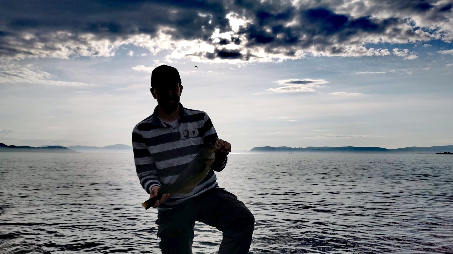 Glücklicher Angler hält einen Dorsch in den Händen, gefangen beim Angeln am Hafen von Hammerfest an den Felsen südlich der Wohnmobilstellplätze
