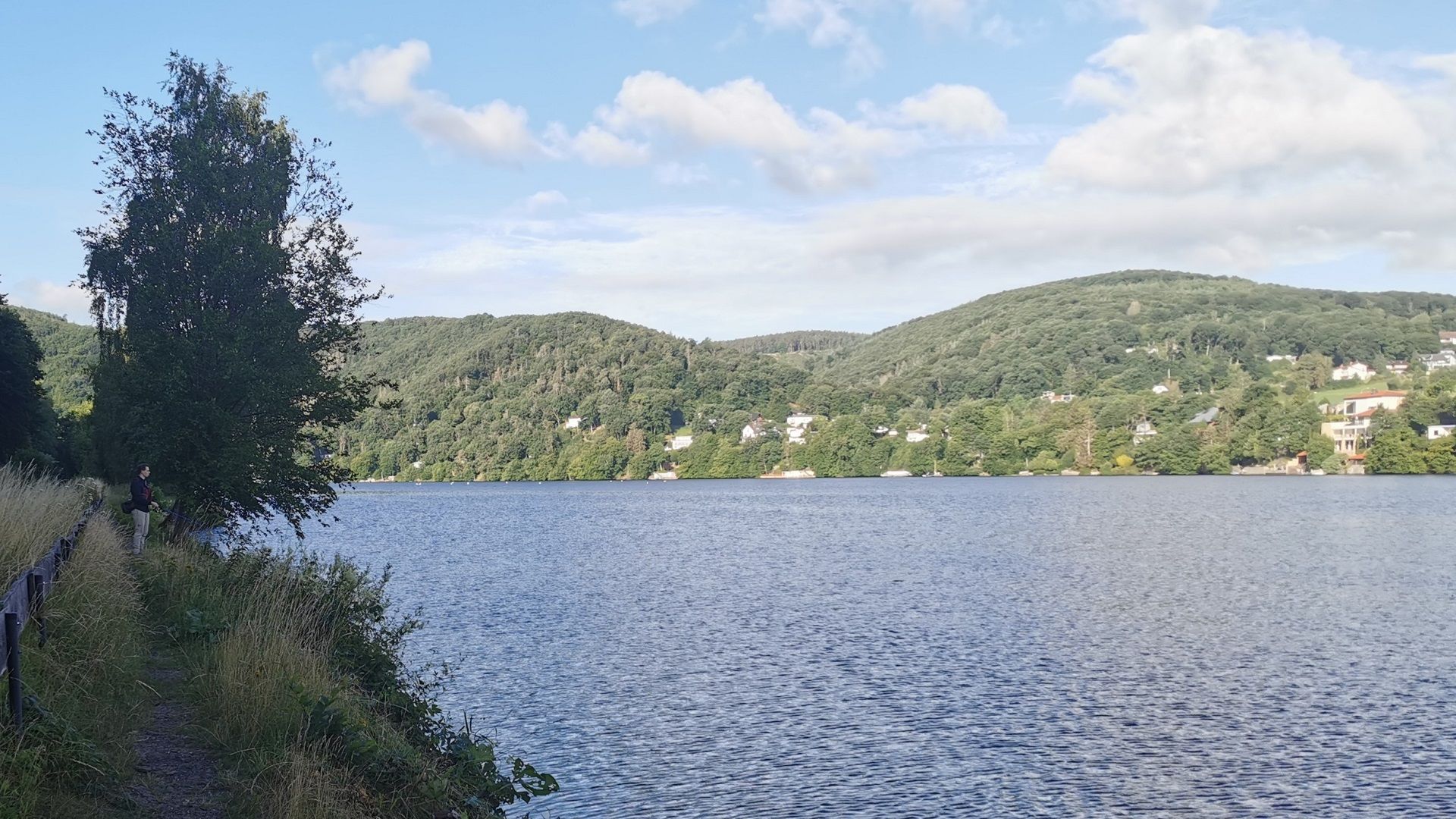 Angler am Staubecken der Rur bei Obermaubach auf dem speziell angelegten Uferpfad am nördlichen Ostufer – das Wasser kräuselt sich leicht im Sonnenlicht, im Hintergrund die bewaldeten Hügel der Voreifel