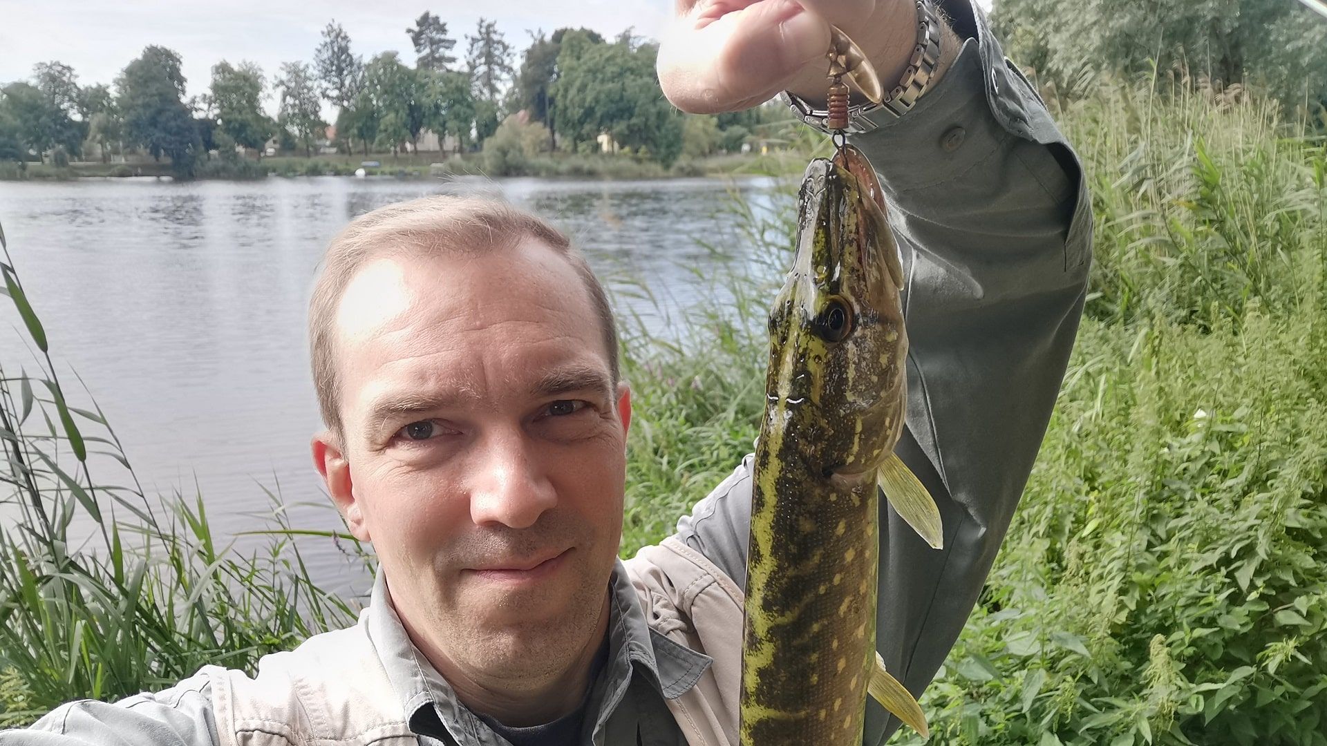 Ein Angler freut sich über einen kleinen Hecht, gefangen mit einem goldenen Mepps-Spinner – erfolgreicher Fang beim Angeln im Mühlensee Liebenwalde.