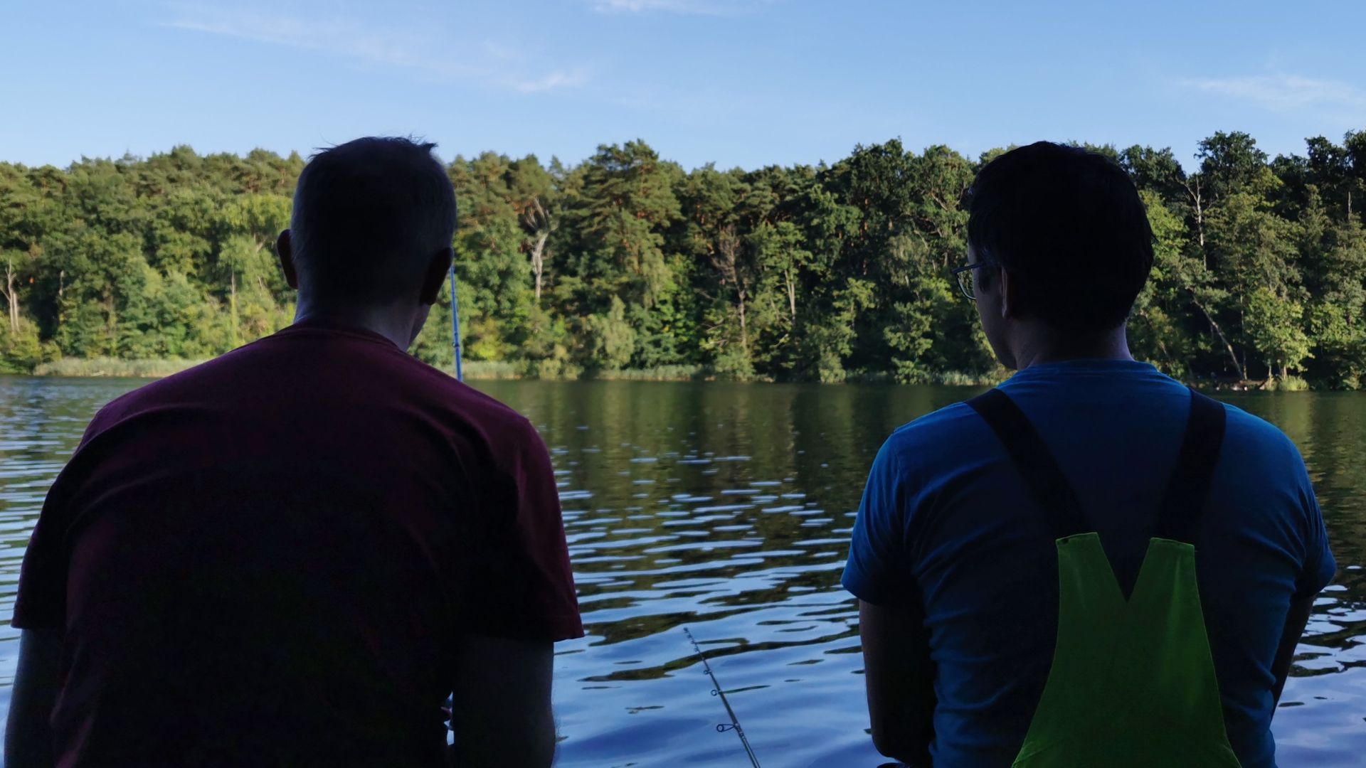Zwei Angelfreunde sitzen entspannt auf einem Steg am Trebuser See, im Gespräch vertieft – ein typischer Moment beim gemeinsamen Angeln in Fürstenwalde.