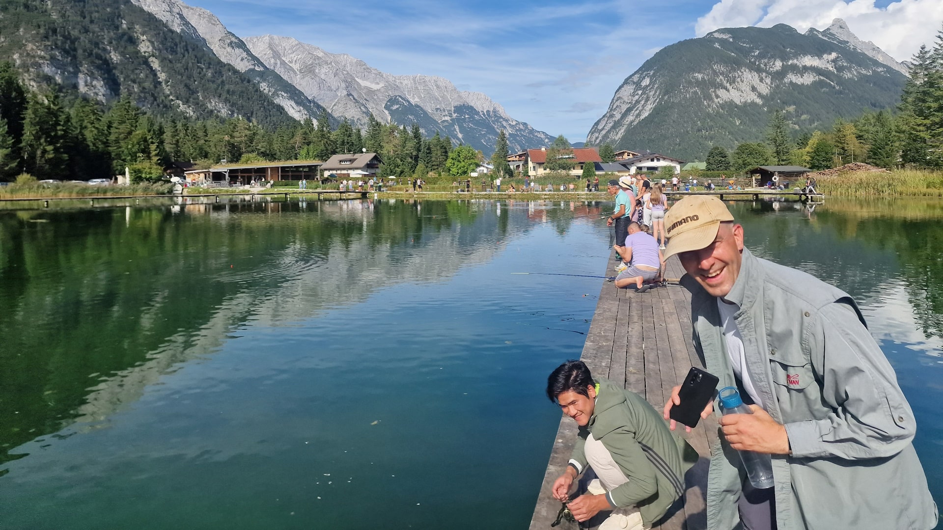 Gruppen von Anglern beim angeln auf den Holzstegen im Weidachsee in Leutasch - mit grüner Wald- und Bergkulisse unter blauem Himmel