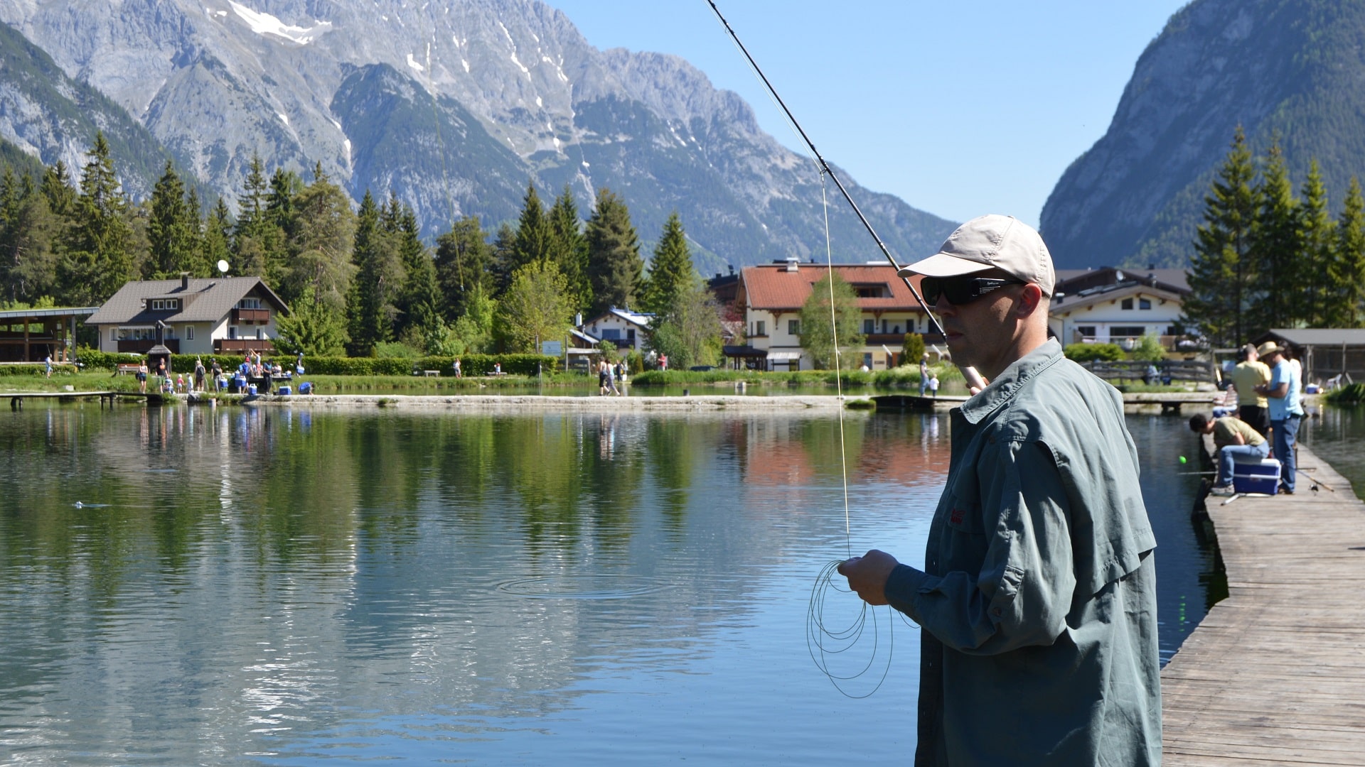 Auch das Fliegenfischen ist möglich beim Angeln im Weidachsee in Leutasch, unter blauem Himmel mit Bergen und Wald im Hintergrund