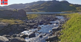 Blick auf den verbindenden Bach zwischen den Bergseen bei Hammerfest mit grünen steinigen Ufern und blauem Himmel. – ideale Naturkulisse zum Angeln