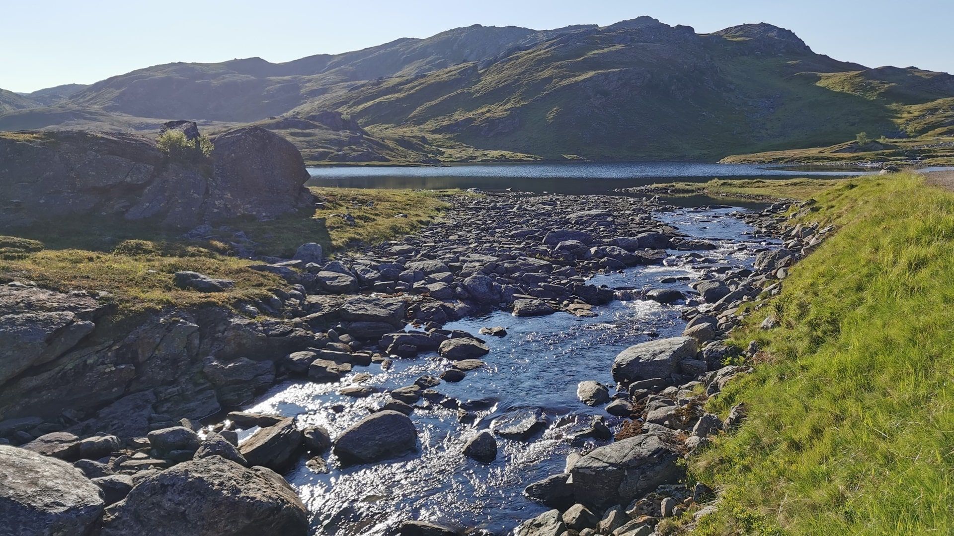 Blick auf den verbindenden Bach zwischen den Bergseen bei Hammerfest mit grünen steinigen Ufern und blauem Himmel. – ideale Naturkulisse zum Angeln