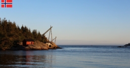 Unter strahlend blauem Himmel bildet eine rote Fischerhütte am gegenüberliegendem Ufer der Mandalselva im Bereich der Mündung ein herrliches Panorama beim Angeln