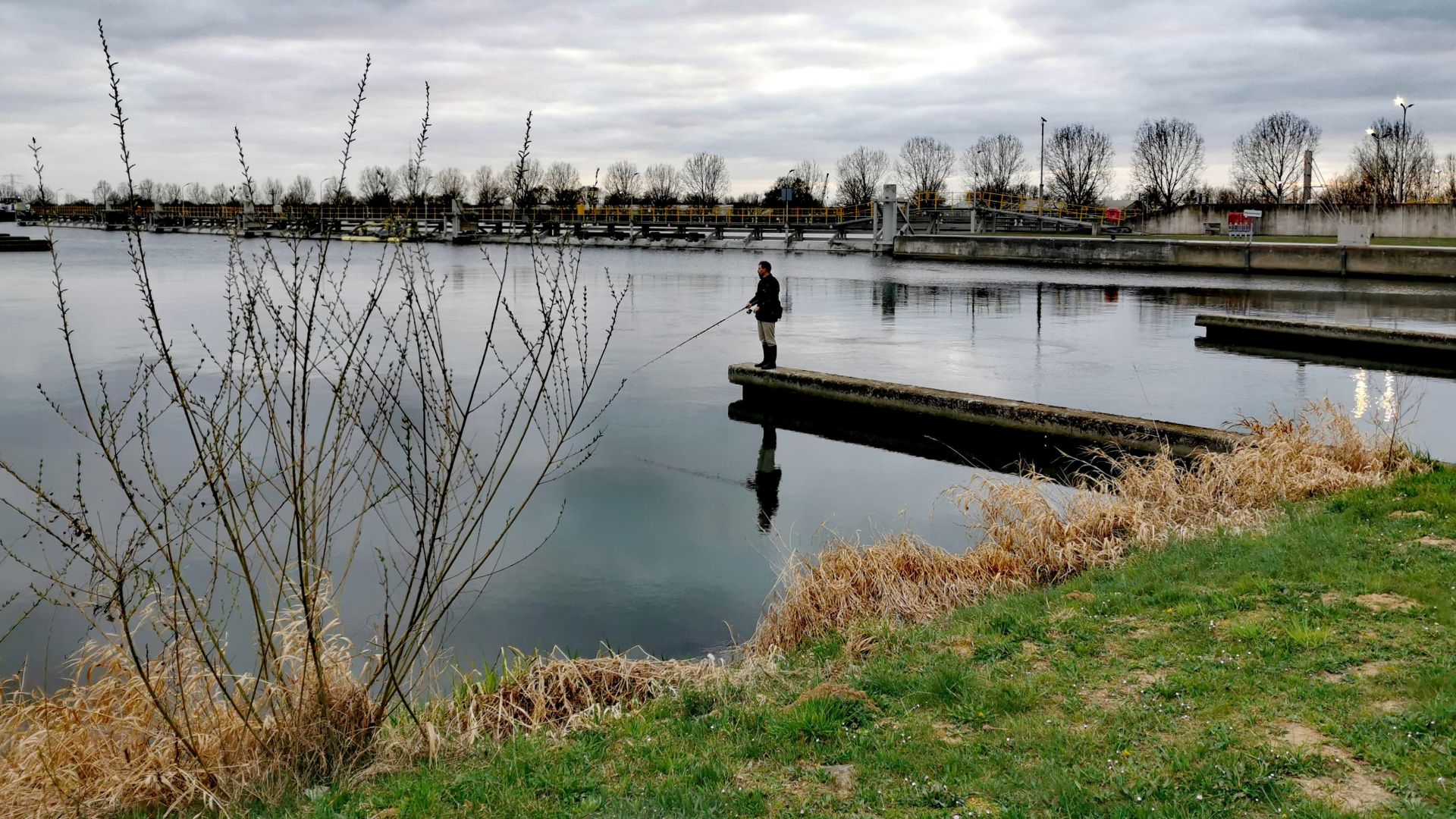 Blick auf den Einlauf am Becken oberhalb der Schleuse in Maasbracht bei Roermond - ein Angler steht auf einer Mauer, an der das Wasser des Schleusenbeckens ins Nebenbecken geleitet wird