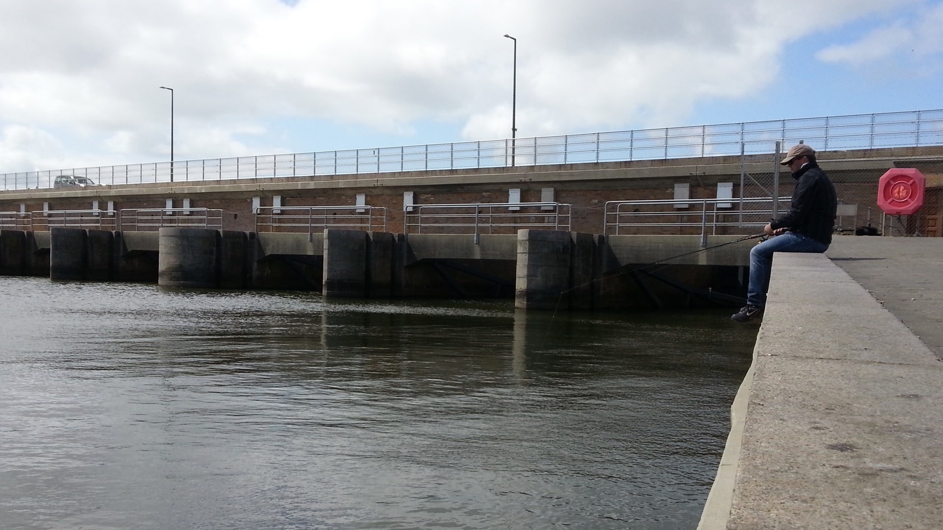 Ein Mann sitzt beim Angeln an der Schleuse in Hvide Sande am befestigten Ufer und wartet darauf, dass sich ein Hornhecht den passiv angebotenen Naturköder schnappt.