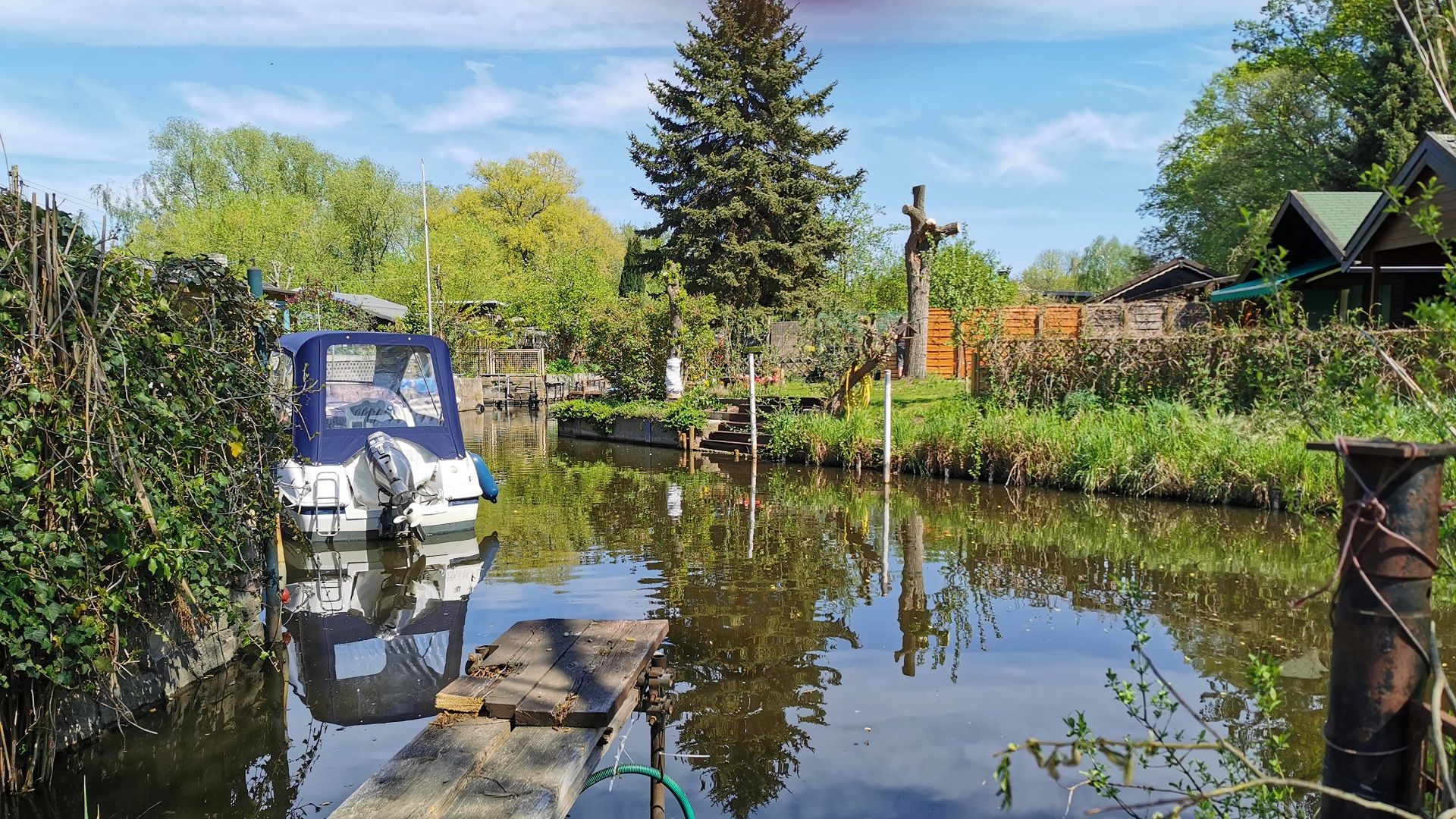 Typische Kulisse beim Angeln in Klein-Venedig inmitten der Tiefwerder Wiesen - Ein Boot liegt an einem kleinen Steg mitten in einer Kleingartenanlage, dichter Uferbewuchs, blauer Himmel und ruhiges Wasser prägen die Atmosphäre