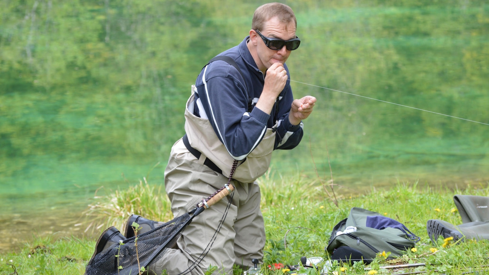 Angler in Wathose bindet einen Streamer an das Vorfach – Vorbereitung zum Angeln mit dem Streamer an der Spinnrute