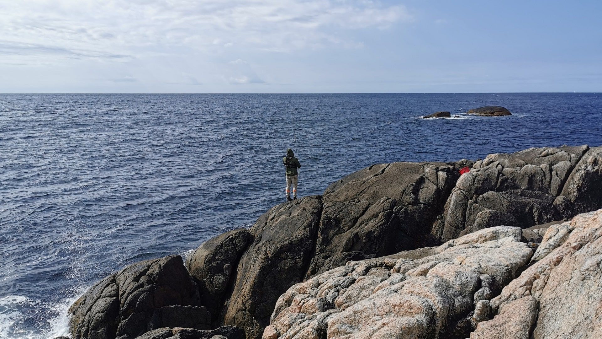Ein Angler mit Küstenspinnrute steht auf dem Felsen am zerklüfteten Ufer von Vågan bei Hauge i Dalane – ein Moment typischer Küstenfischerei beim hiesigen Angeln