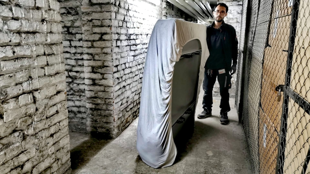Freund im Keller hält das in ein weißes Laken gewickelte Dachzelt fest – erster Schritt der Dachzelt-Montage vor der Angelsaison.