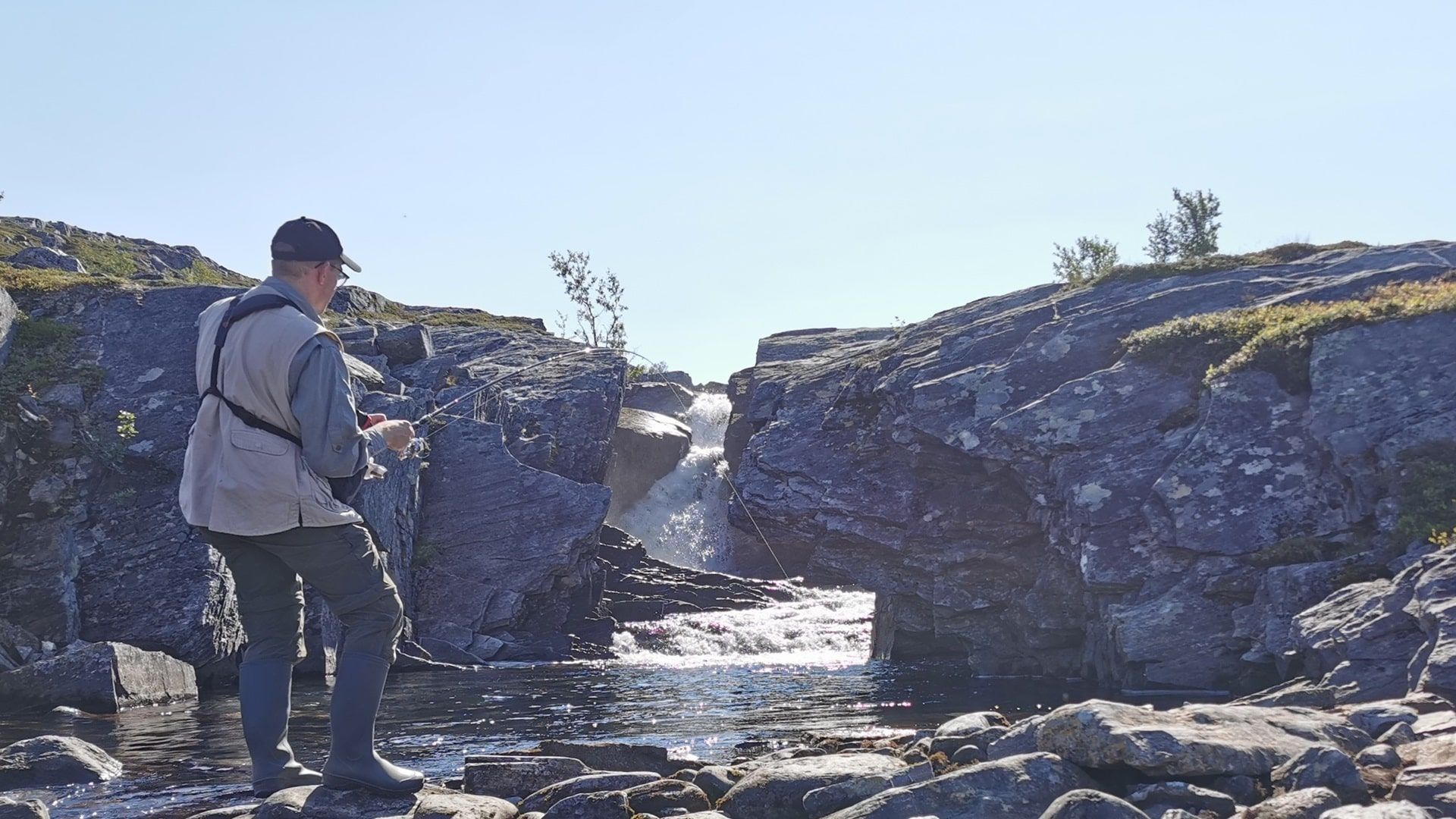 Ein Angler im Drill beim Fischen mit dem Spinner in einem klaren Bergbach – gezieltes Werfen in Gumpen erfordert Übung, lohnt sich aber beim Angeln auf Forelle und Saibling mit Spinner