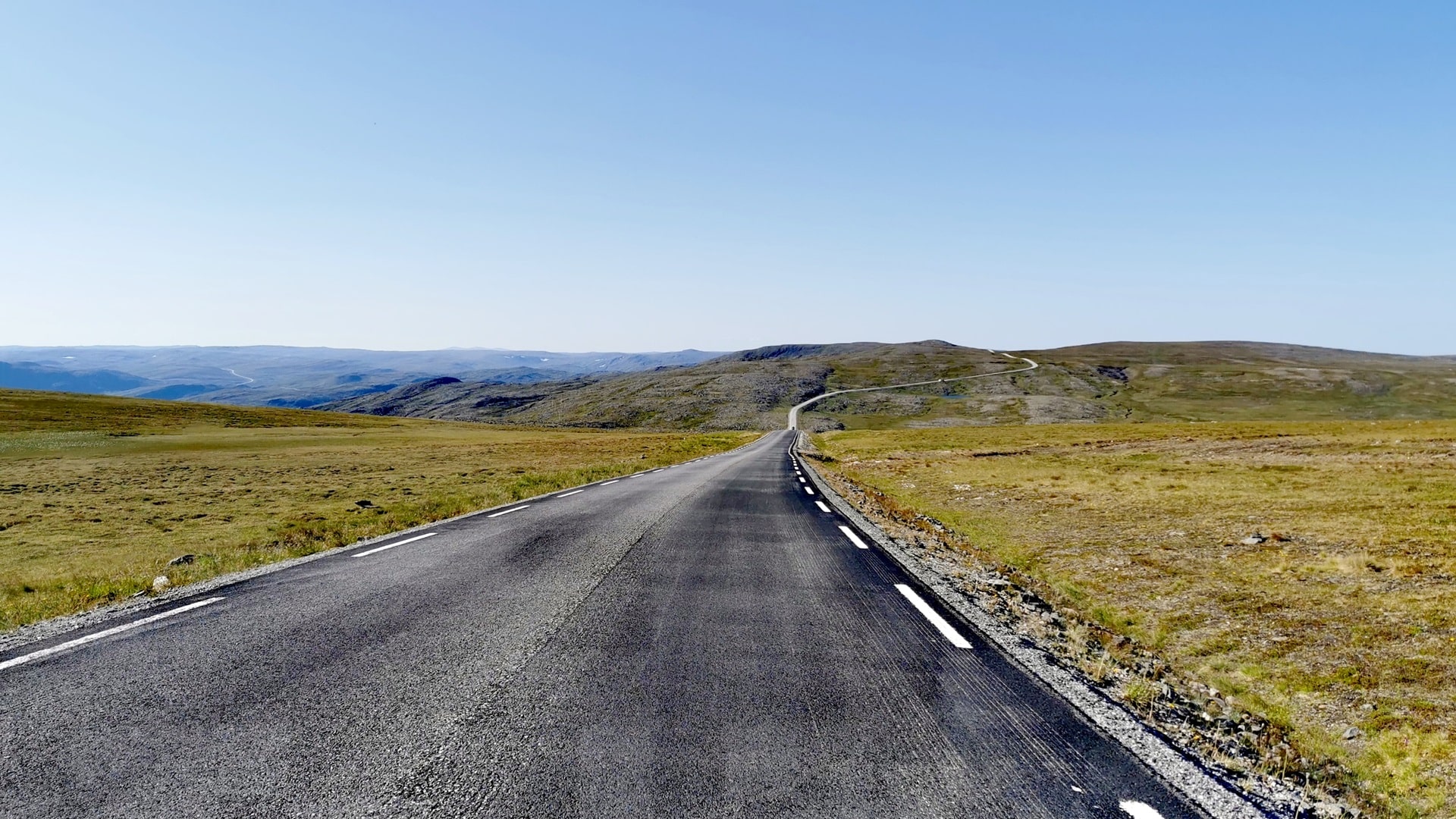 Straße zum Nordkap durch karge grüne Landschaft mit weitem Blick unter wolkenlosem Himmel