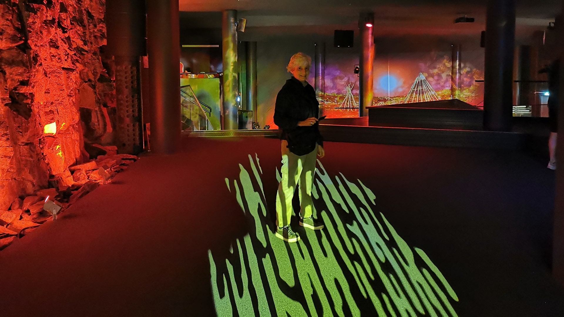 Frau steht im Zentrum des faszinierenden Lichterspiels in der Cave of Lights der Nordkaphalle