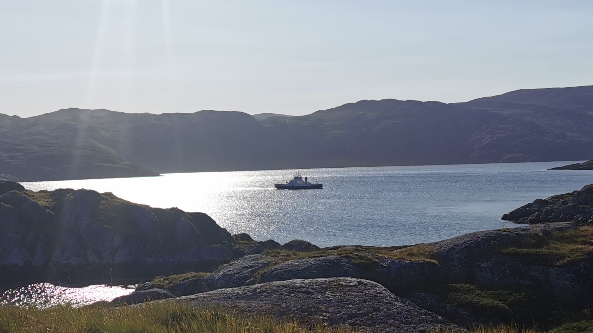 Fähre auf dem Weg zur Insel Seiland im Abendlicht, tiefstehende Sonne über ruhigem Wasser und unter klarem, blauem Himmel