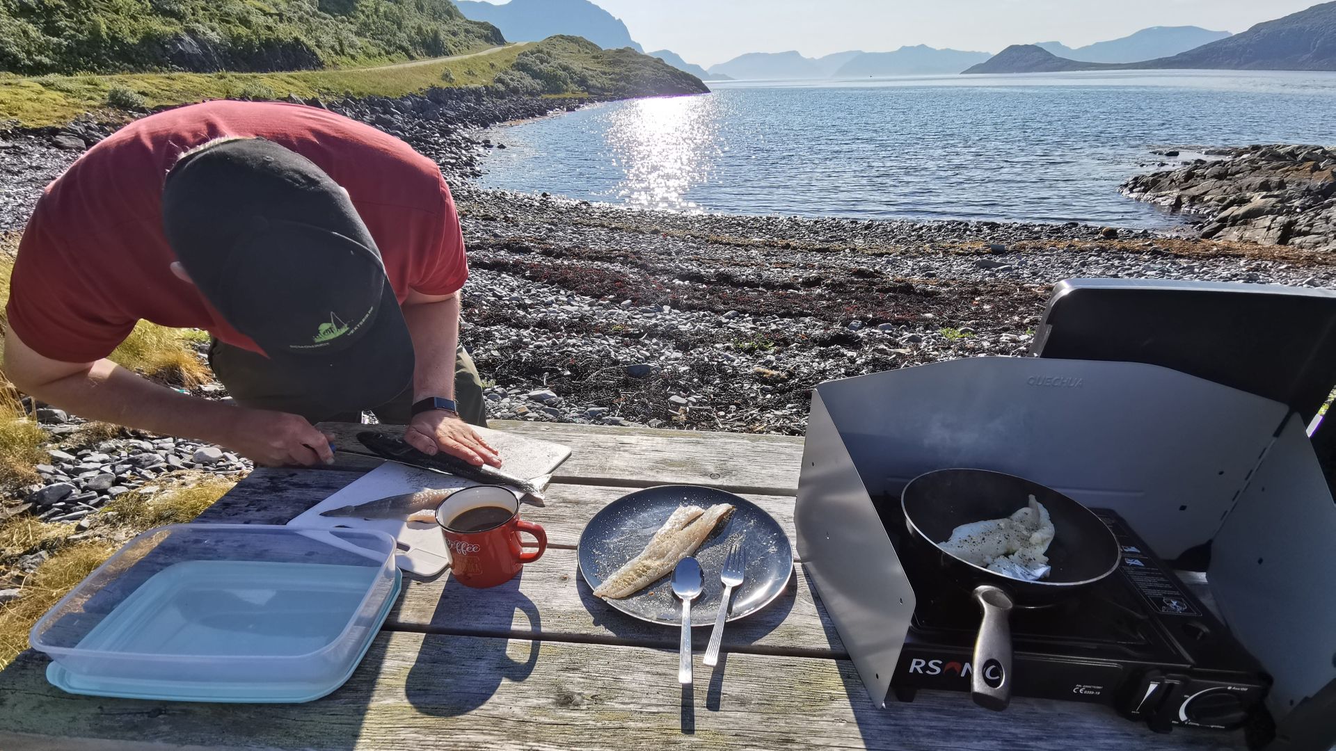 Ein Angler filetiert seinen frisch gefangenen Fisch bei der Scenic Picnic Area auf Seiland – klarer Himmel und ruhige Atmosphäre am Wasser
