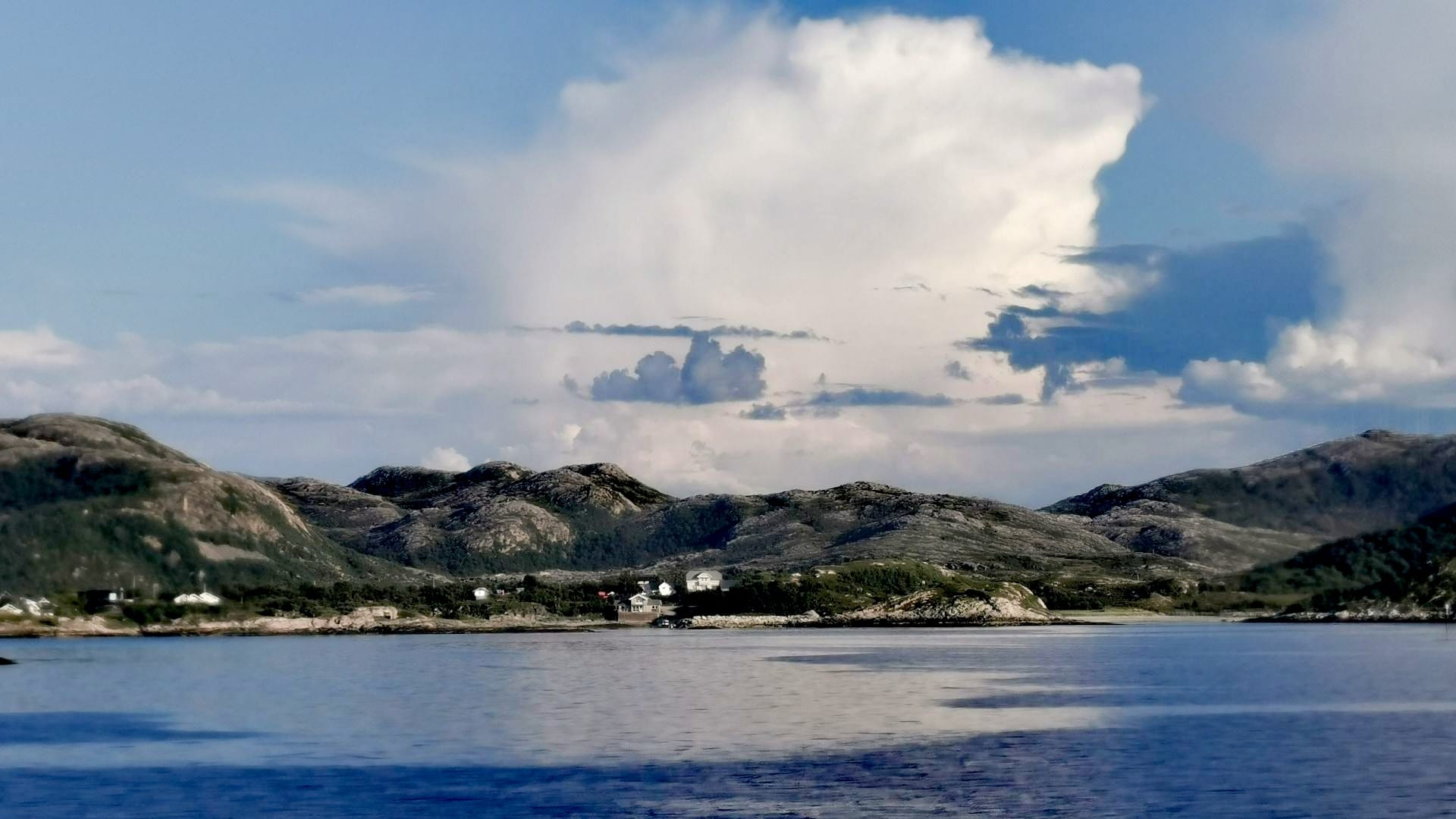 Blick vom Fähranleger Brensholmen über das ruhige, blaue Meer bei leicht bewölktem Himmel auf die Küstenhügel