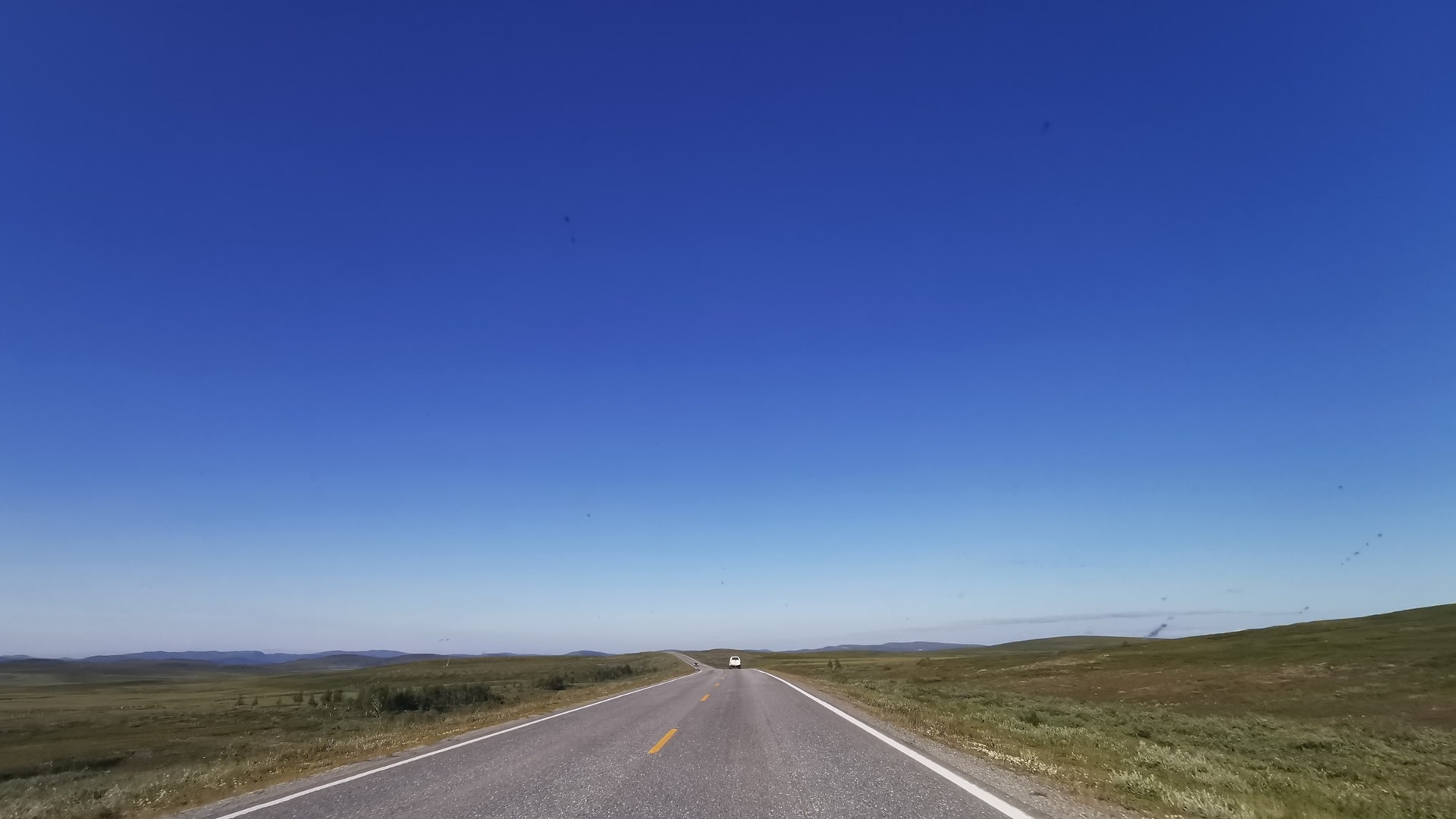 Unendlich wirkende Straße durch die weite, karge Landschaft Lapplands bei bestem Wetter