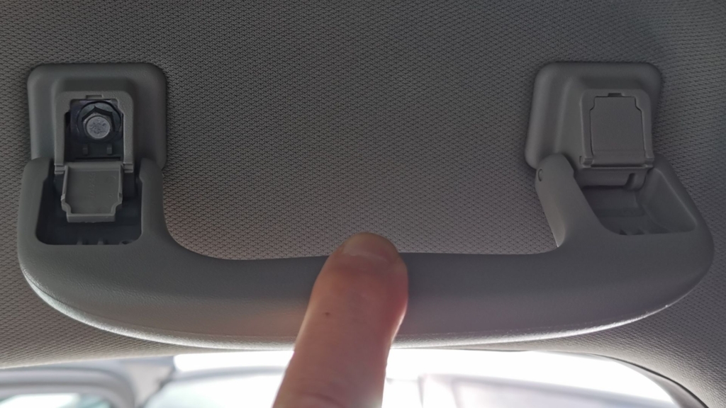 Nahaufnahme eines Angstgriffs im Auto – kleine Kunststoffklappen geben die Schrauben zur Demontage frei.