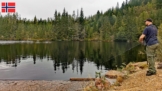 Angler beim Angeln oberhalb der Staumauer des Flekkerøvann bei Skien, spiegelglattes Wasser, rötlicher Felsboden und von Mischwald gesäumtes Ufer