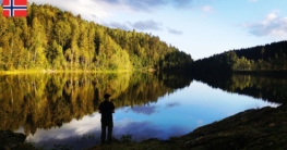 Spiegelglatter Stulvann bei Skien mit Angler am Nordufer, tiefstehender Sonne und frühherbstlich gelb-grünen Laubbäumen, die sich im Wasser spiegeln