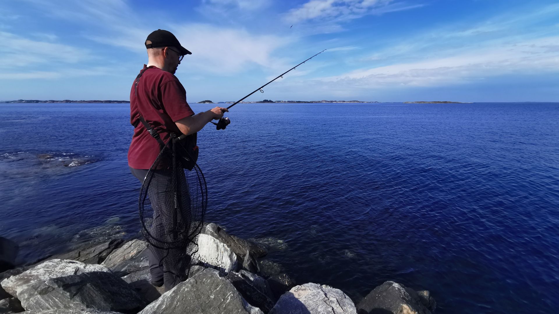 Angler steht am felsigen Ufer von Hellesøy, Sotra, mit Blick nach Norden auf das Meer – typische Szene beim Angeln in der Region Bergen