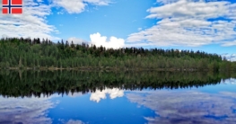 Blick über den spiegelglatten Lona bei Skien an einem sonnigen Tag, blauer Himmel mit wenigen Wolken und Nadelwald, der sich perfekt im Wasser spiegelt