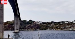 Angler beim Angeln am Rongesundet auf Sotra bei Bergen, winzig klein auf dem Sockel der imposanten Brücke, gegenüber typische norwegische Häuser am Ufer