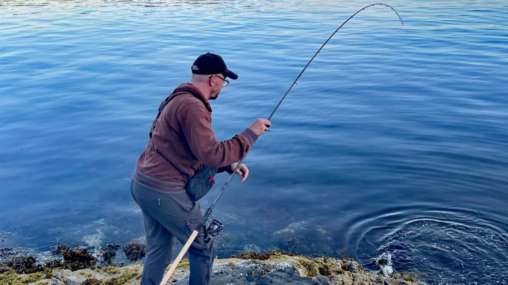 Autor hält den Blank der Savage Gear Parabellum CCS 10'1 Test-Rute mittig mit der rechten Hand, um einen gehakten Fisch an felsiger Uferstelle zu landen.