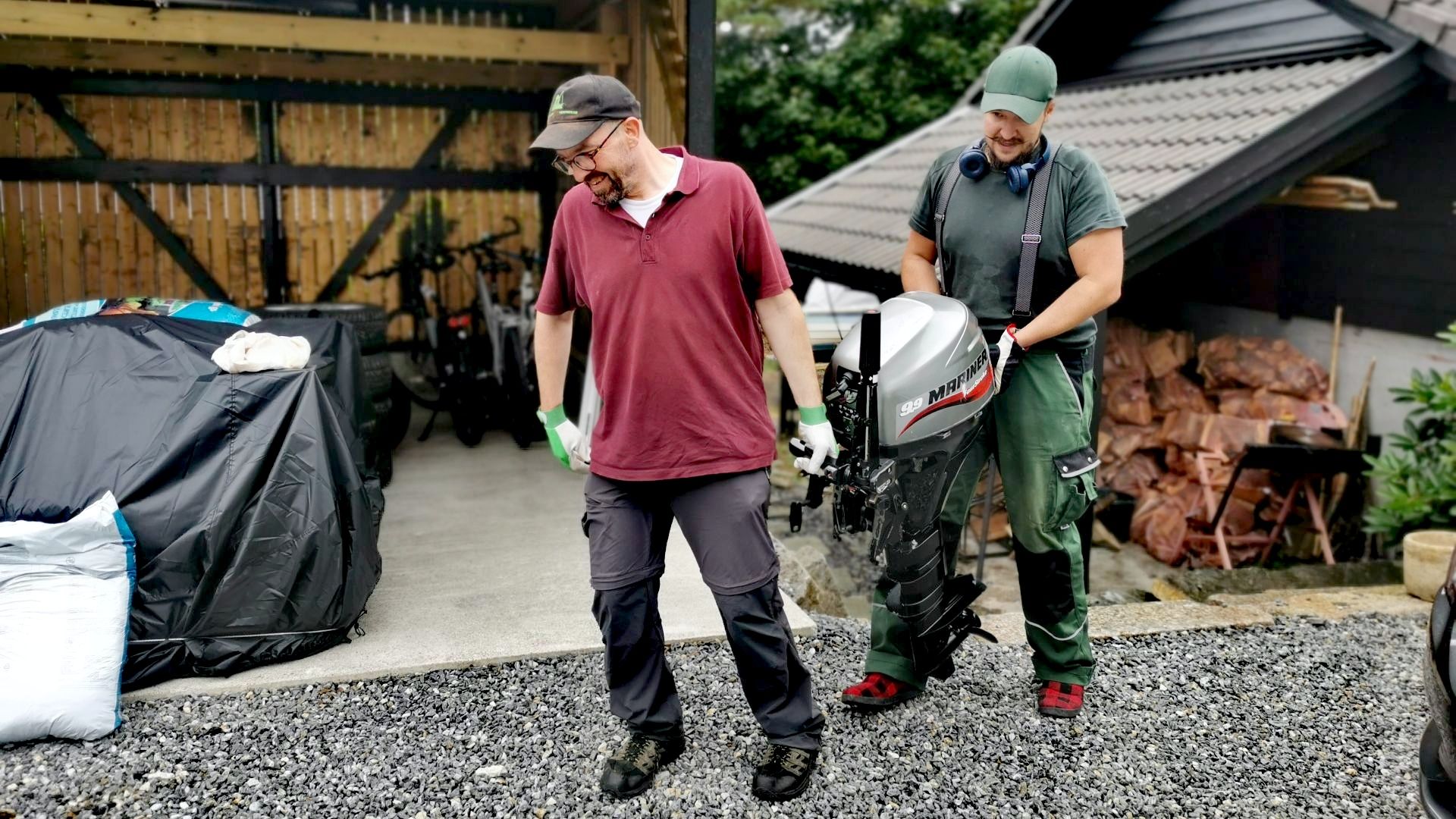 Zwei Männer tragen einen defekten Schiffsmotor in eine Garage – Zwischenstopp während der Angeln mit Dachzelt Tour rund um Bergen