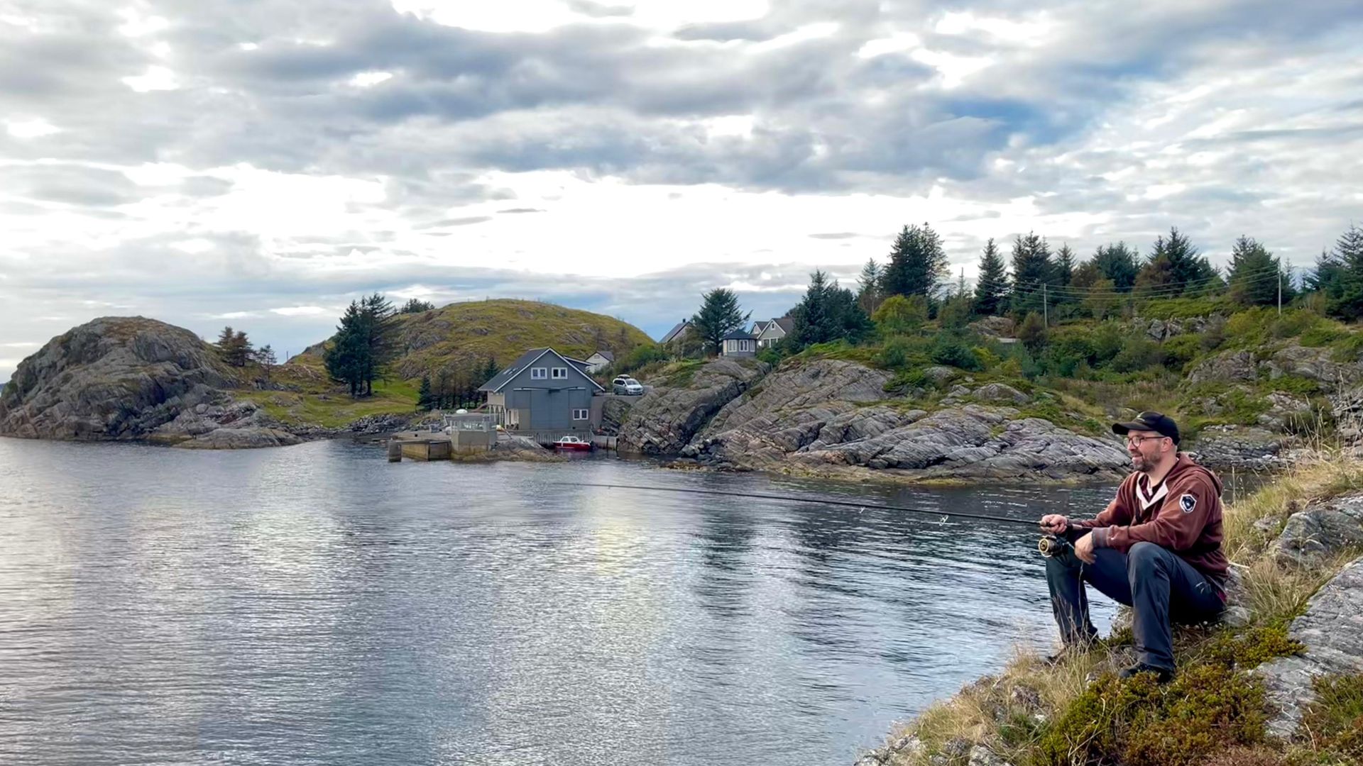 Angler sitzt entspannt auf Felsen und pilkert eine tiefe Stelle ab – typische Szene beim Angeln mit Dachzelt nahe Bergen