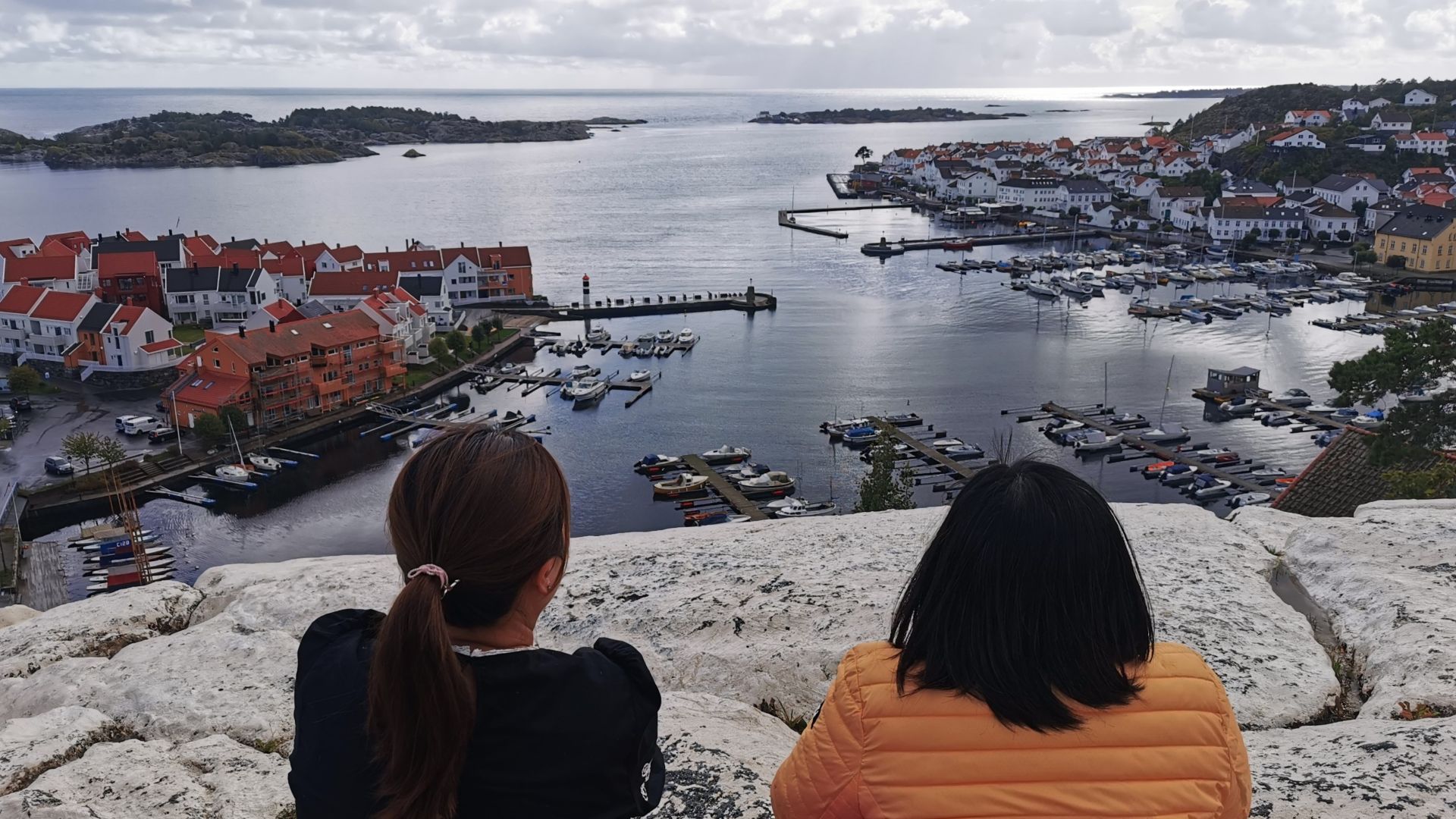 Zwei Frauen sitzen auf einem Felsen oberhalb von Risør und schauen über den Ort, den Hafen und die vorgelagerten Inseln aufs offene Meer.