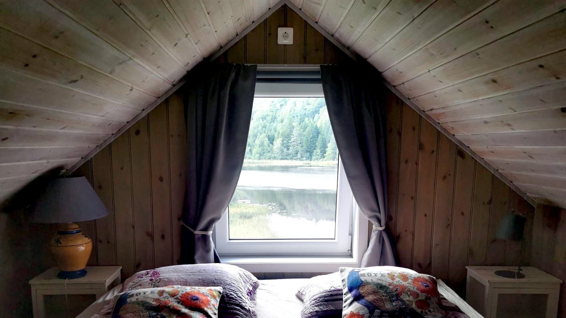 Blick aus dem Fenster unter der Dachschräge unserer Unterkunft in Risør direkt auf den See; unter dem Fenster steht das Bett.