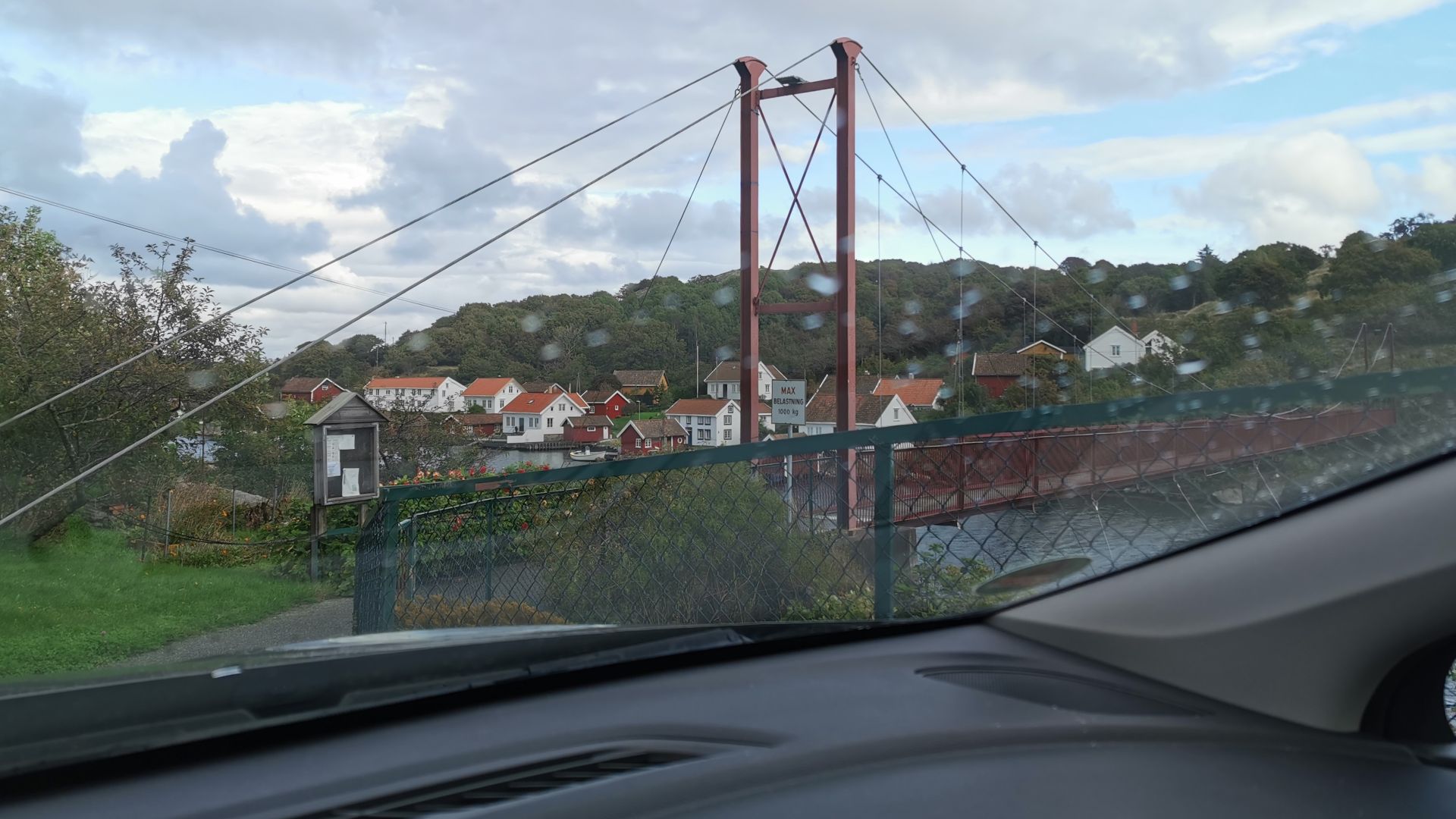 Rote Fußgänger-Hängebrücke im Süden der Insel Skjernøya bei Mandal unter leicht bewölktem, aufgelockertem Himmel.