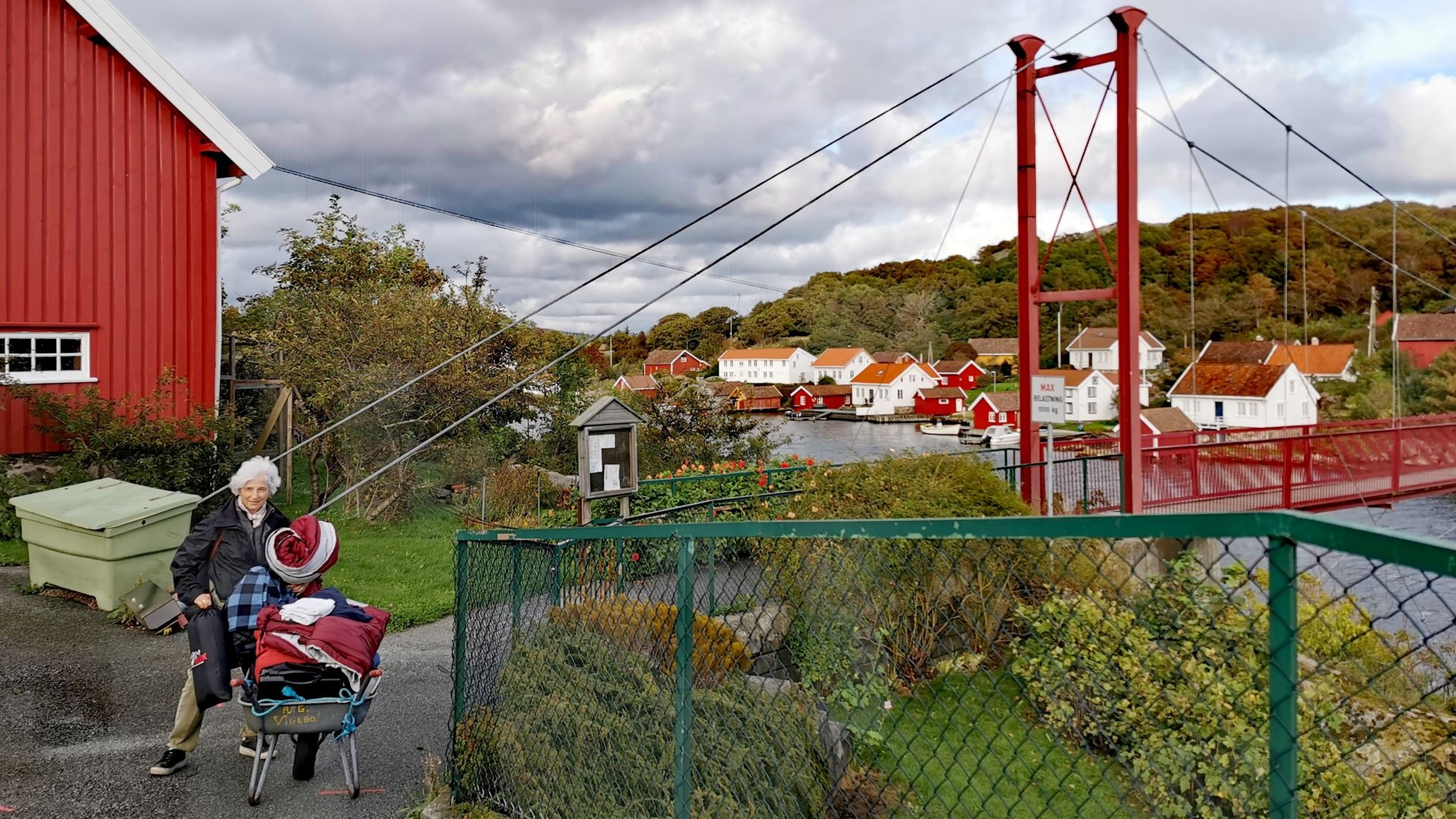 Frau schiebt eine Schubkarre voller Gepäck zur gebuchten Hütte auf Skjernøya, da die rote Hängebrücke nicht befahrbar ist.