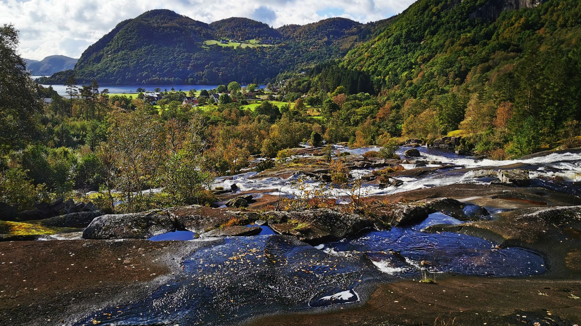Blick über die wasserreichen Kaskaden bei Drange mit bewaldeten Hügeln, Talblick und Fjordbucht in der Ferne