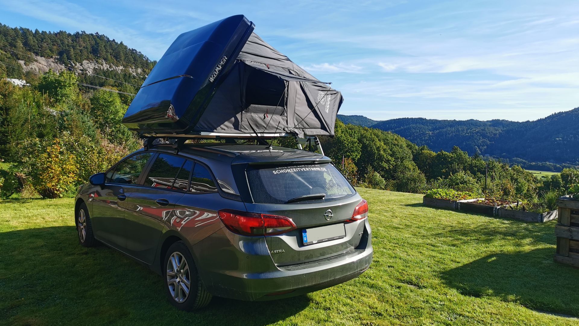 Auto mit aufgebautem Dachzelt iKamper Skycamp Mini 3.0 auf einer Rasenfläche bei Sonnenschein mit Blick über ein norwegisches Tal